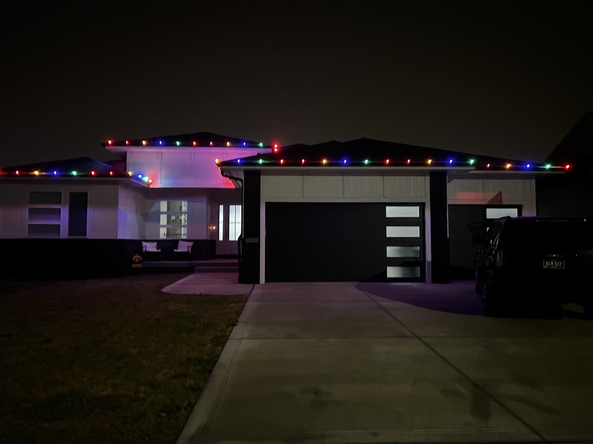 Multicolor C9 bulbs spaced evenly along a roofline and garage peak on a winter evening